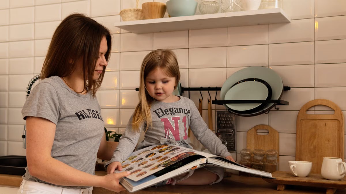 A mother and daughter enjoy reading a cookbook in a modern kitchen, sharing fun and learning together.