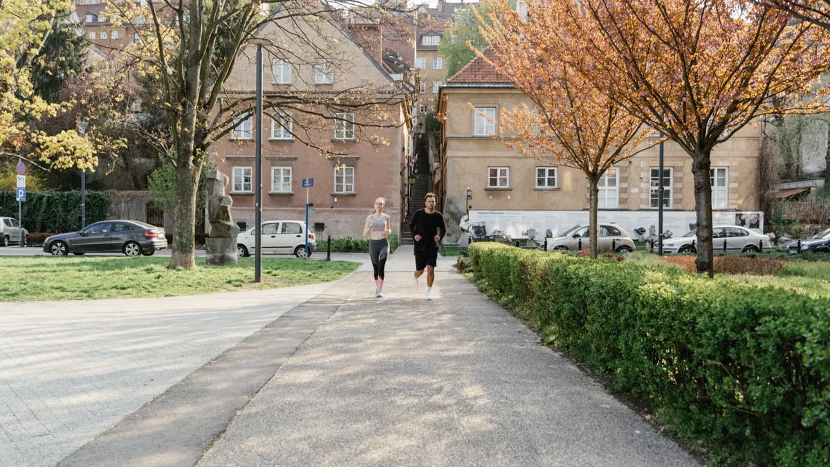 A couple jogging together in an urban park surrounded by greenery and houses.